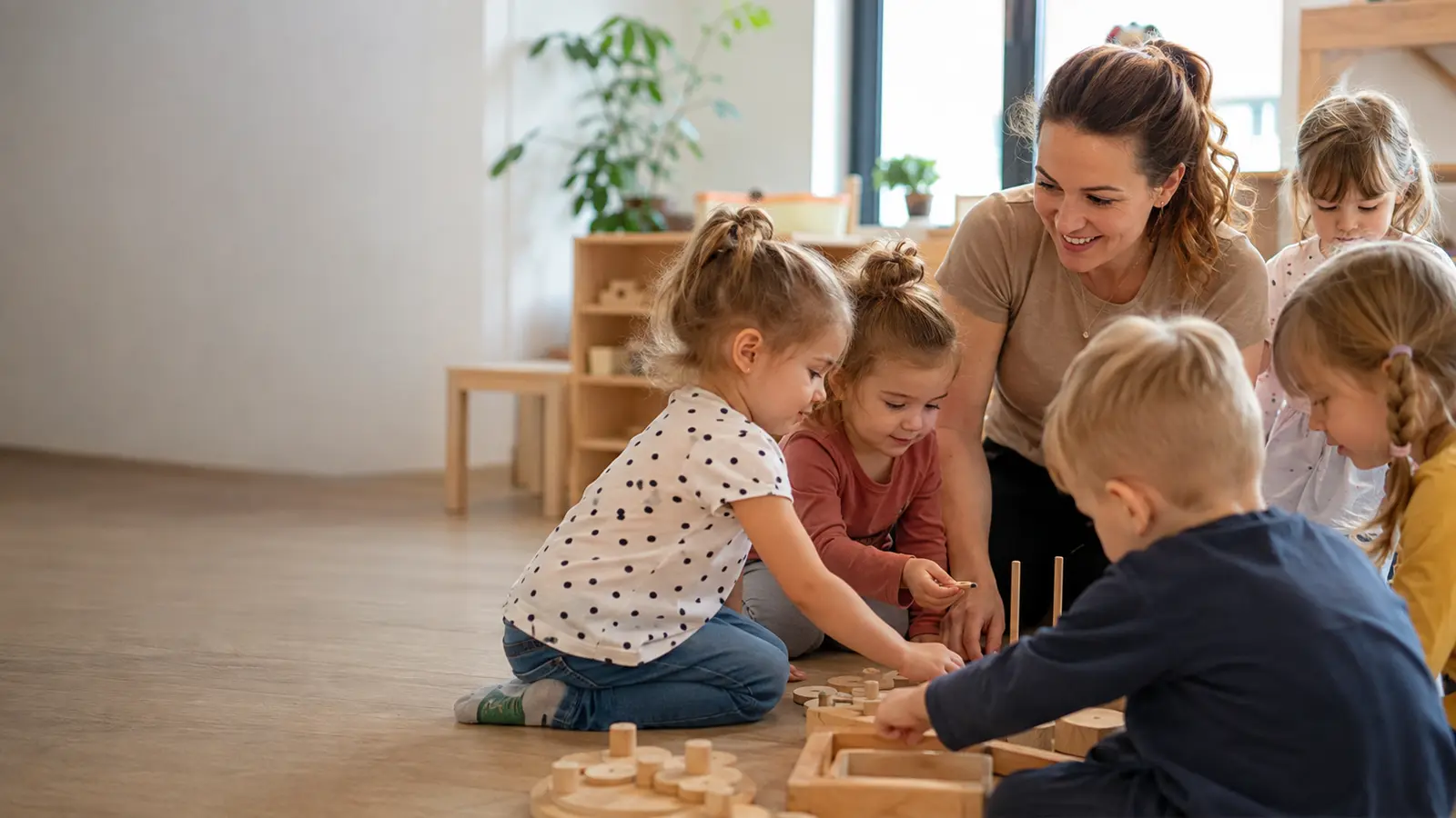 Opiekunka i dzieci podczas wspólnej zabawy edukacyjnej w jasnej sali żłobka